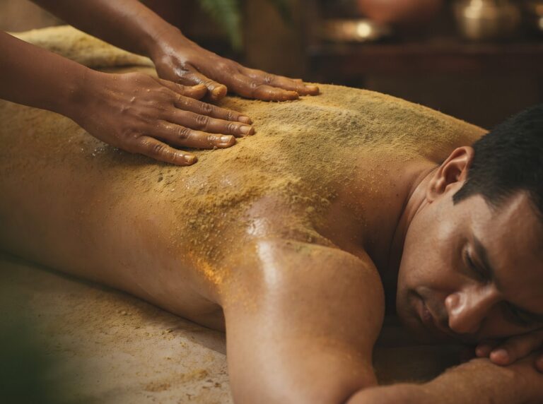 Therapist massaging the back with dry herbal powder during Udvartana