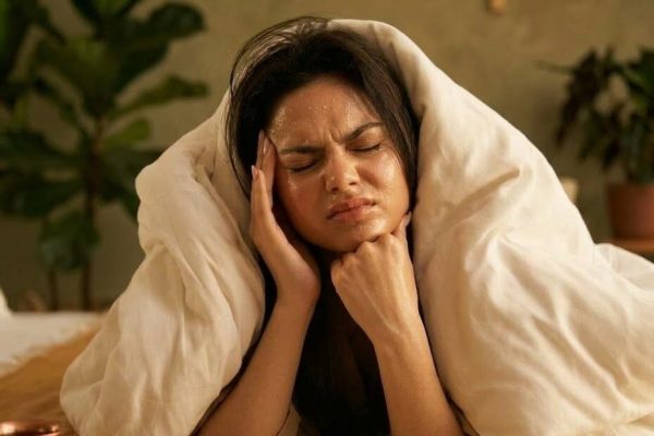 Woman holding her head in pain, wrapped in a blanket